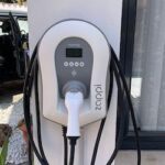 A Tesla electric vehicle charging station mounted on a wall with a charging cable plugged in.