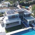 A modern white villa with solar panels on the roof, a swimming pool, and green lawn areas.