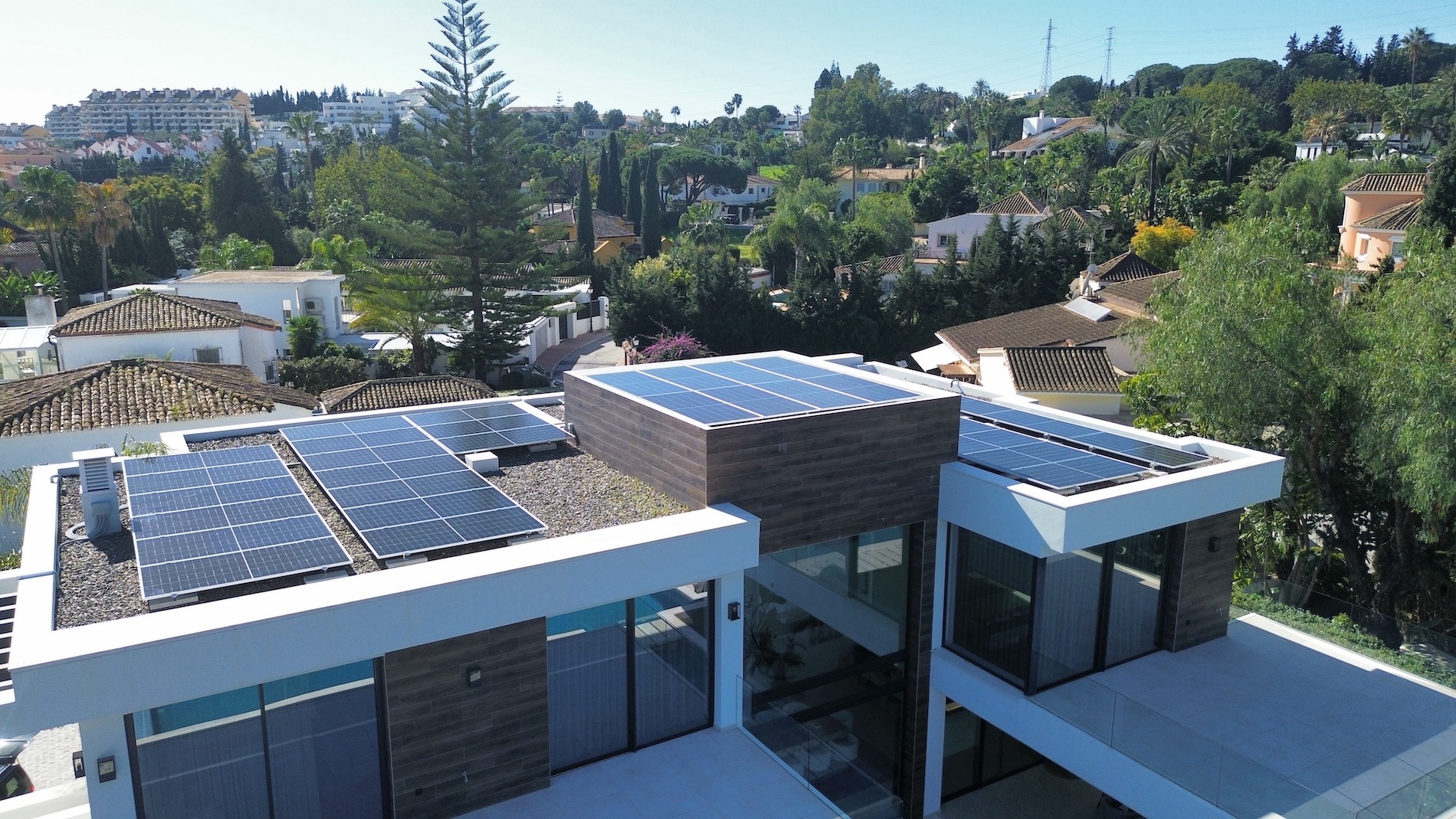 A modern house with solar panels installed on the roof under a clear sky in a suburban neighborhood.