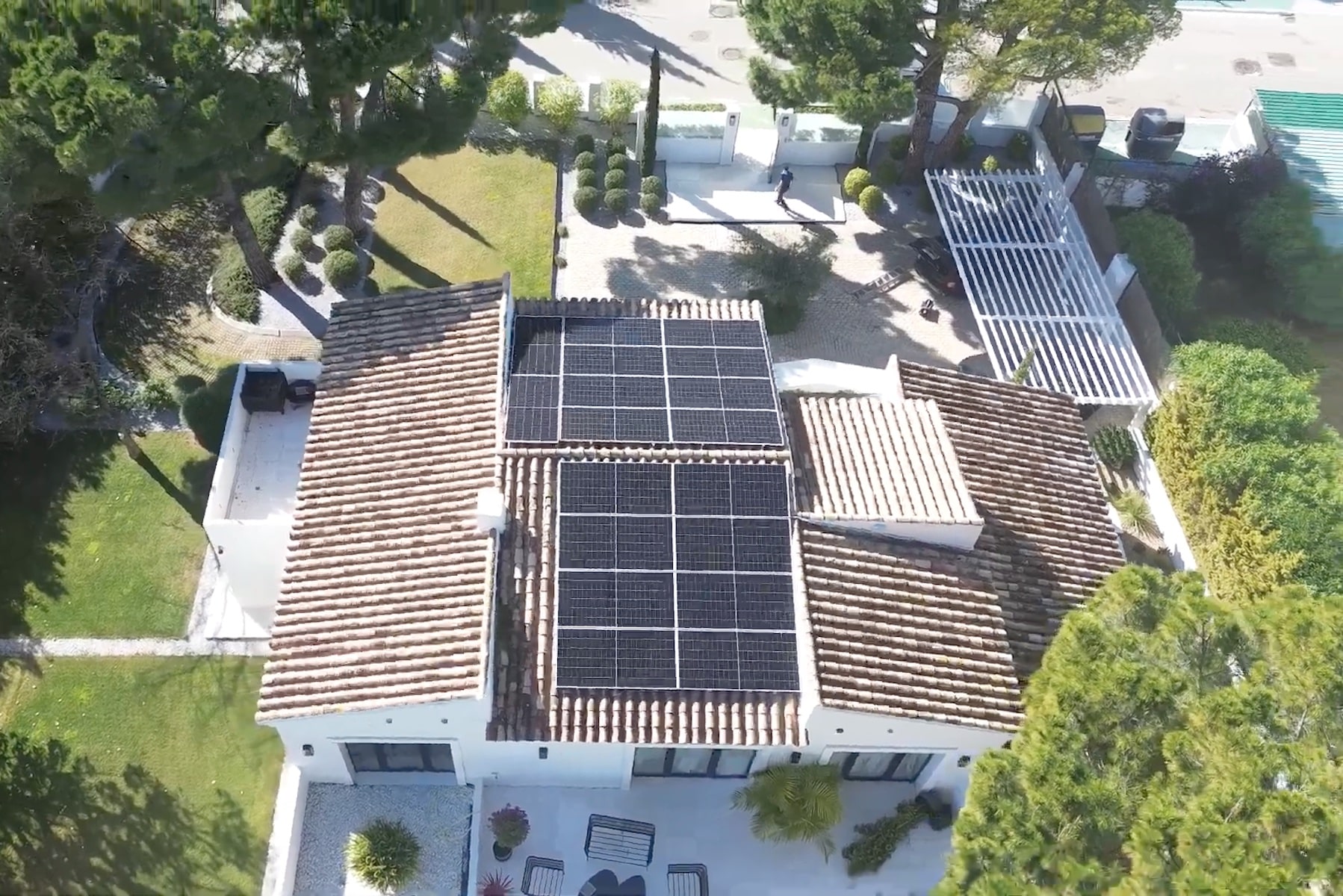Aerial view of a house roof equipped with solar panels surrounded by trees and a patio area.