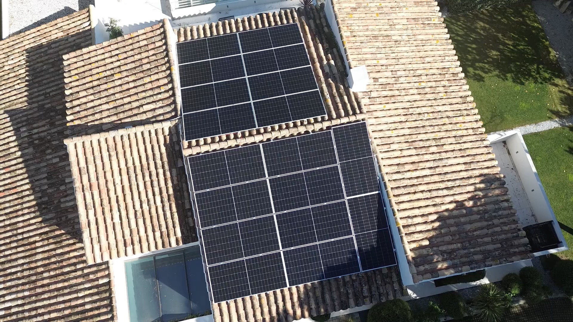 Two solar panel arrays installed on a brown tiled rooftop under sunlight.
