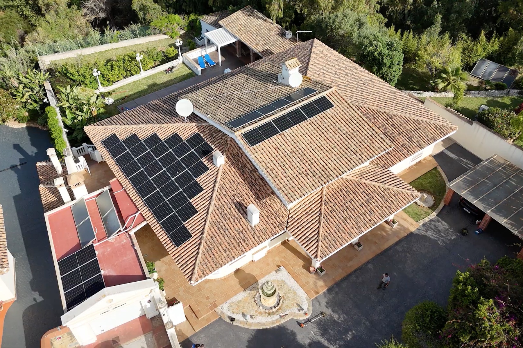 Vista aérea del tejado de una casa con paneles solares instalados en un lado y rodeada de vegetación.