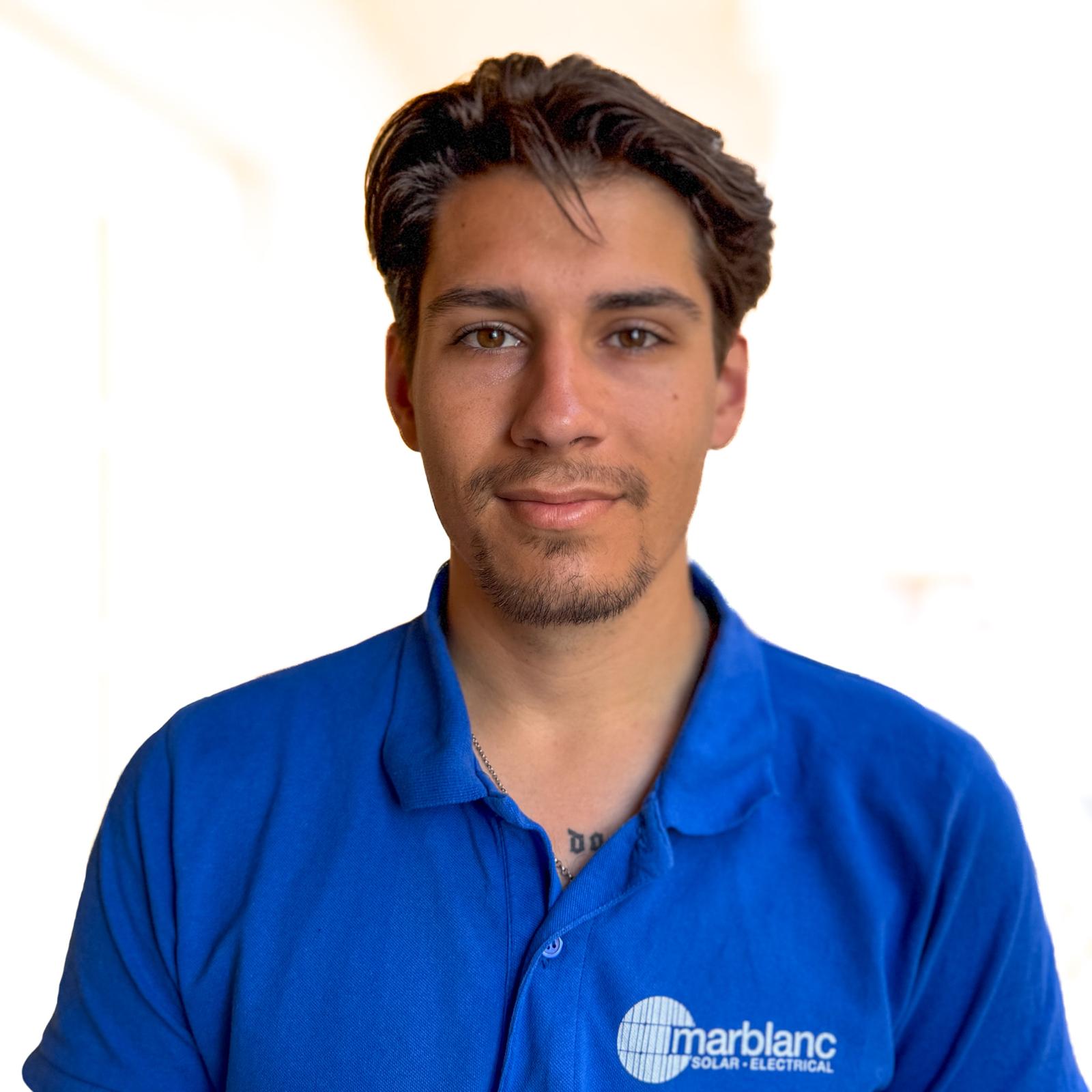 Portrait of a young man with short brown hair wearing a blue polo shirt against a white background.