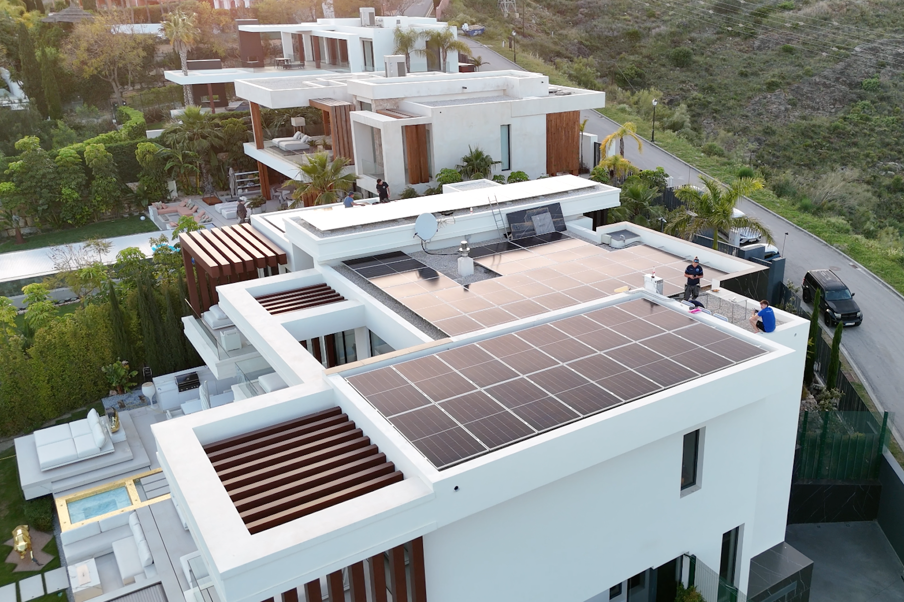 Modern white buildings with rooftop solar panels in a green, hilly area under sunlight.
