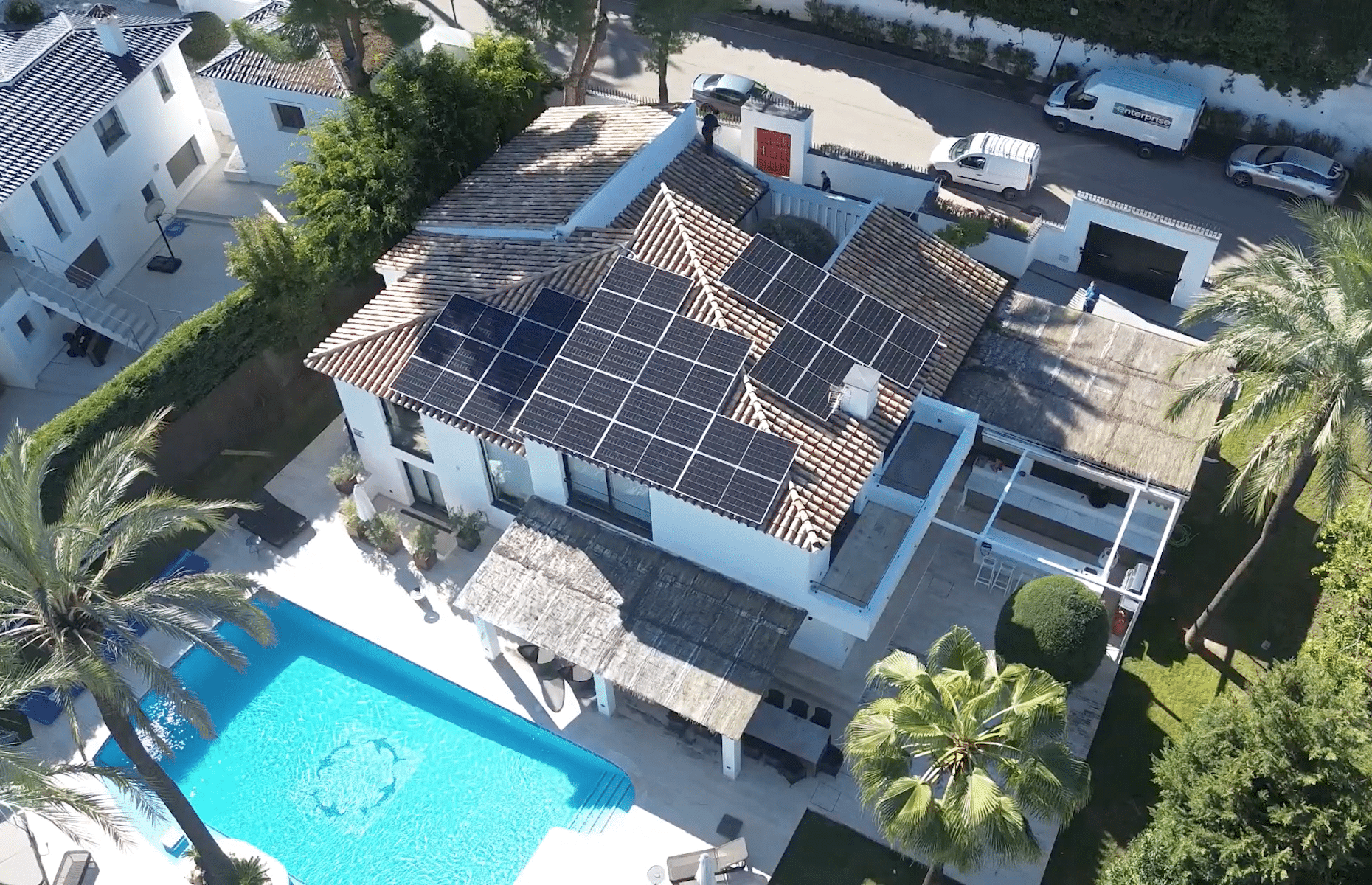Aerial view of a modern two-story house with solar panels on the roof and a swimming pool in the backyard.