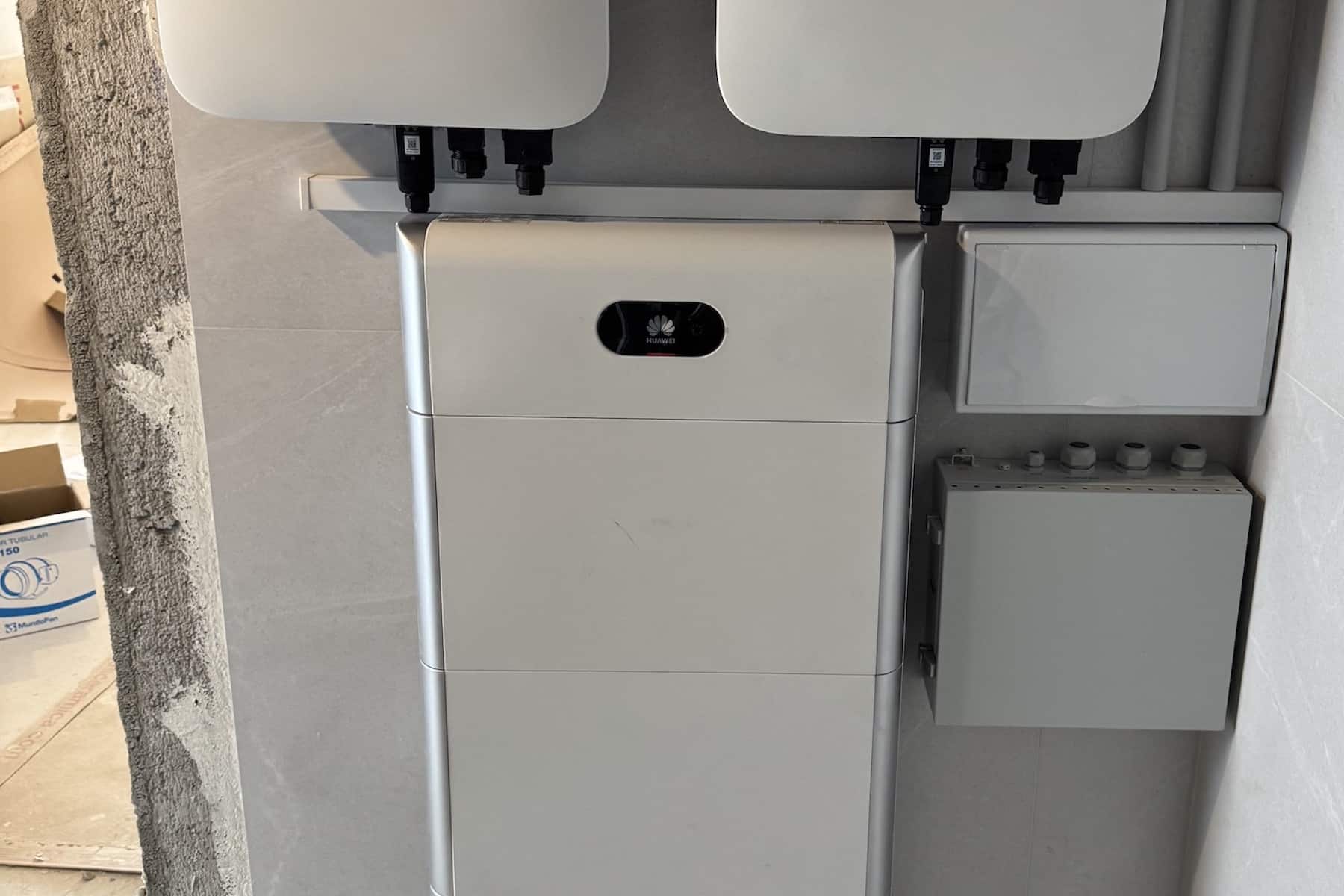 A white wall-mounted device with a small black display panel, flanked by two white panels and a power cable on the left.